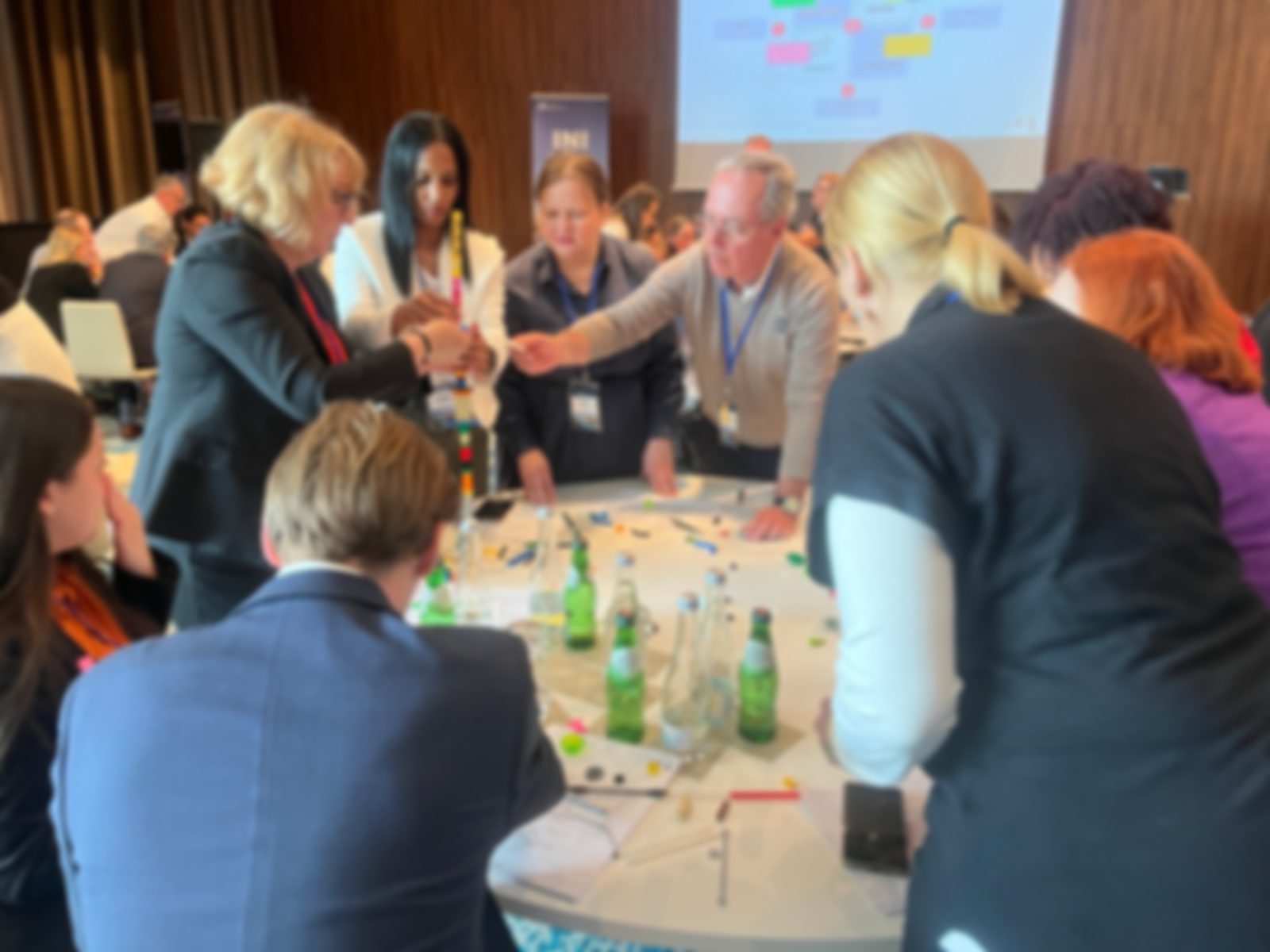 Gruppe von Fachleuten mit Namensschildern arbeitet an einem runden Tisch bei einem interaktiven Konferenzformat zusammen