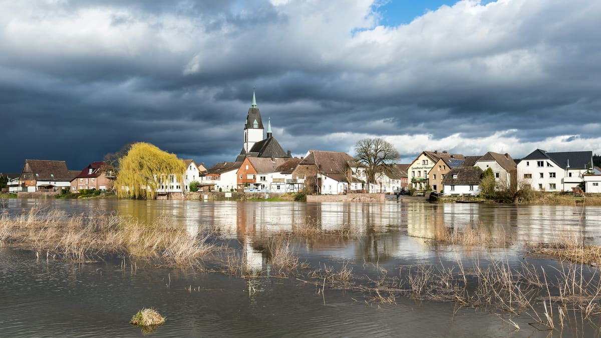Hochwasser in einem Dorf an der Weser, im Hintergrund die Kirche unter dunklem Himmel