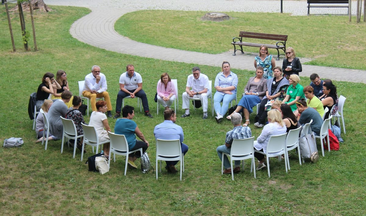 Menschen sitzen im Kreis auf Stühlen auf einer Wiese und sprechen miteinander